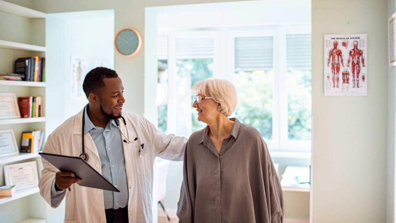 Un jeune médecin accompagne sa patiente vers la porte à la fin de la consultation.