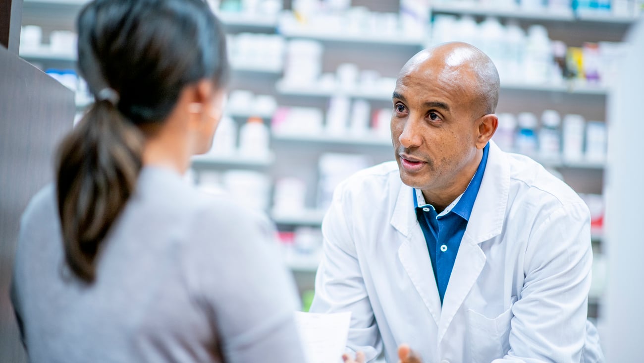 Pharmacien derrière son comptoir en train de discuter avec une patiente.