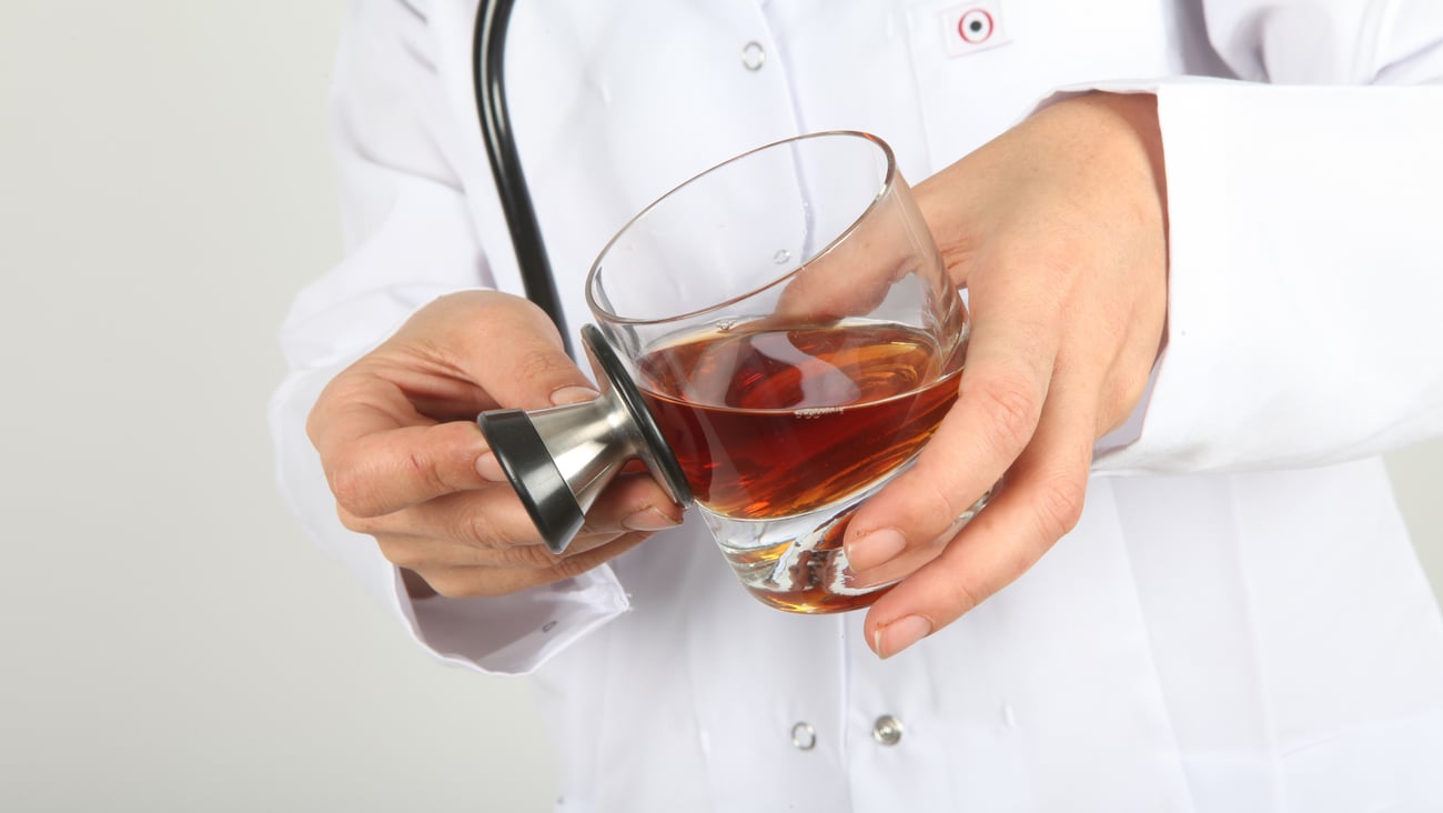 Médecin tenant un verre de whisky dans sa main.