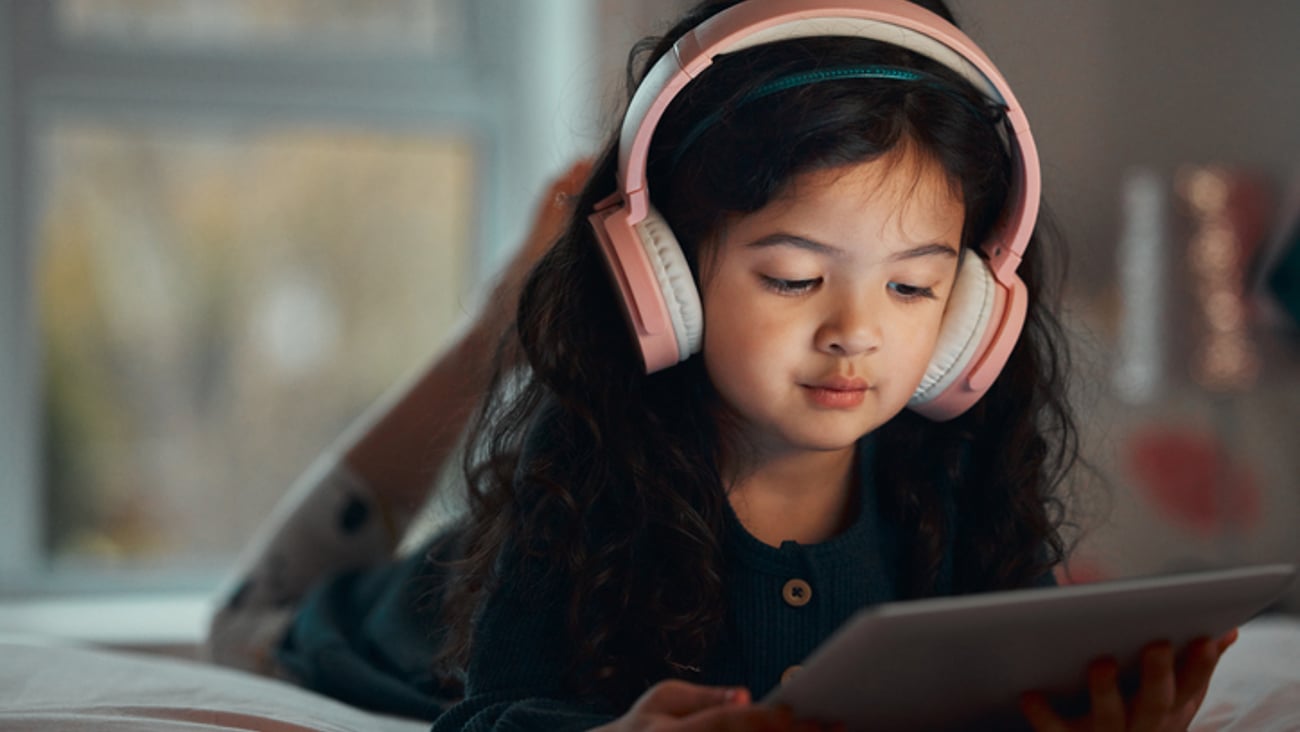 Une enfant sur son lit est devant sa tablette