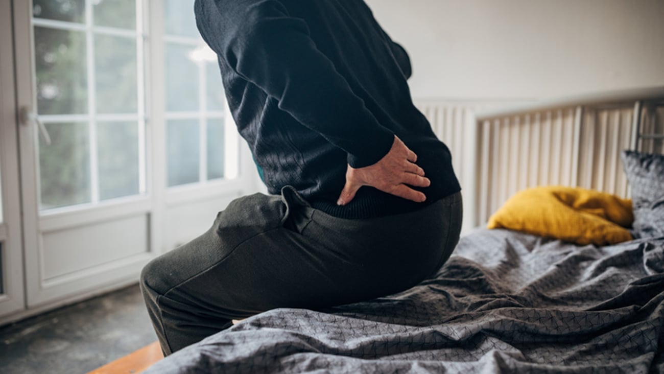 Un homme qui se lève de son lit a un mal de dos.