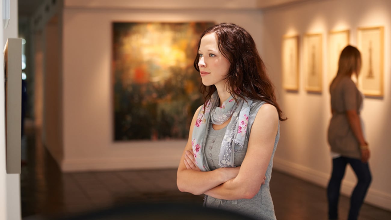 Une femme heureuse est en train de regarder une oeuvre d'art dans un musée.