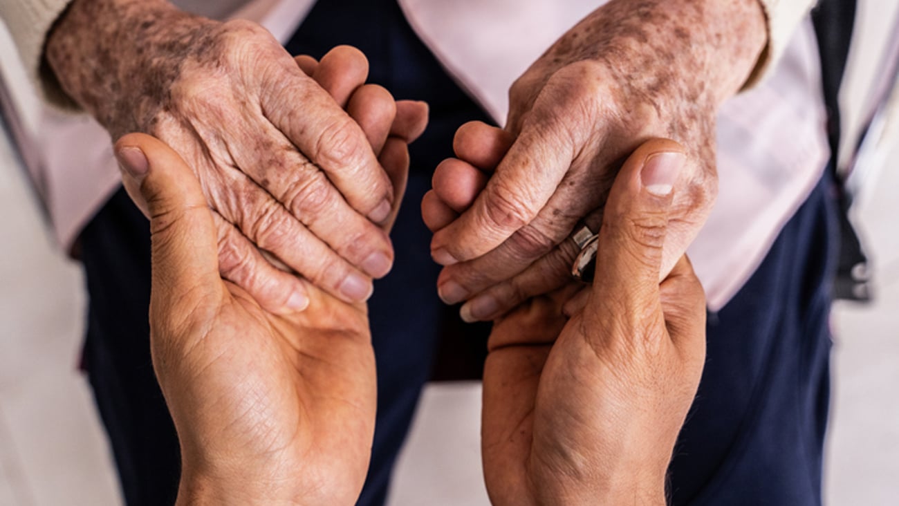 Un soignant tient les mains d'une personne âgée.