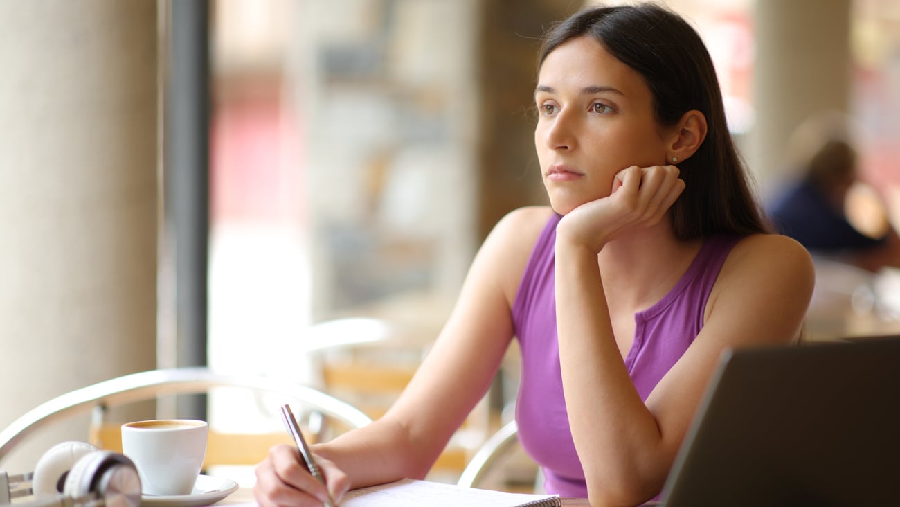 Caucasion woman sitting inside cafe gazing off into distance