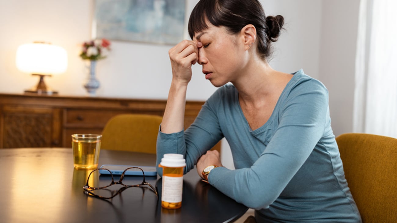 Une femme assise à une table a mal à la tête, et vient de prendre des médicaments.