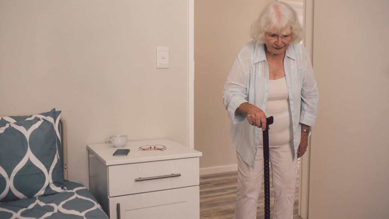 Une personne âgée marche avec une canne en se dirigeant vers sa chambre.