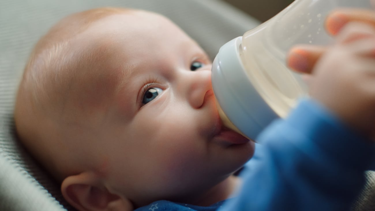 Un bébé boit au biberon, en vue rapprochée.