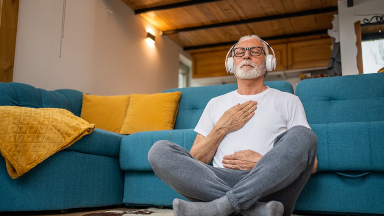 Un homme médite dans son salon avec des écouteurs sur les oreilles.