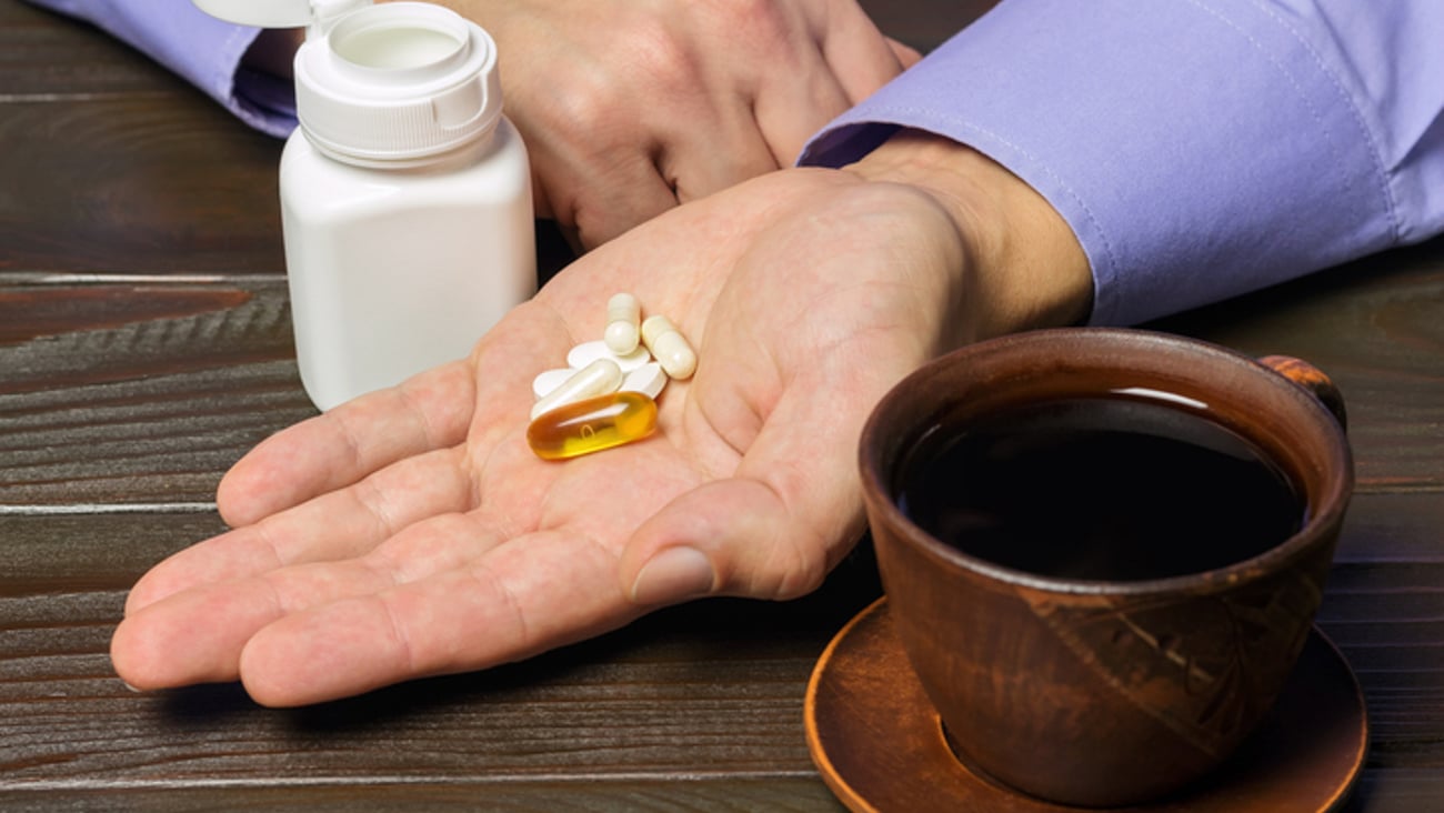 Une personne tient des médicaments dans sa main à côté d'une tasse de café