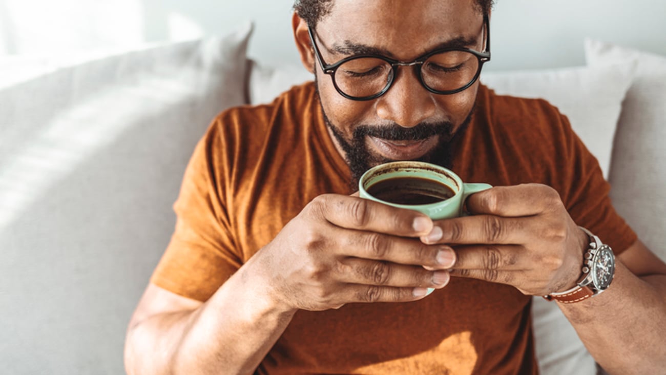 Un homme sourit et boit une tasse de café