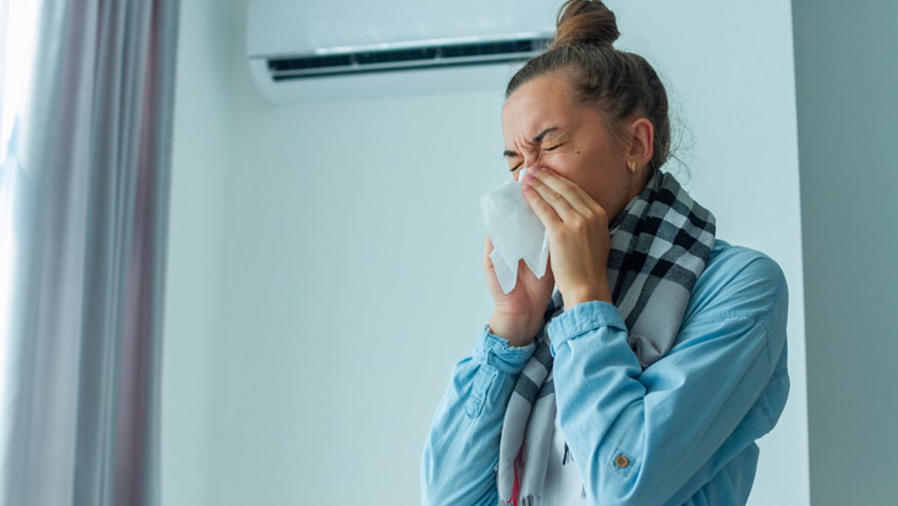 Une jeune femme se mouche devant un climatiseur