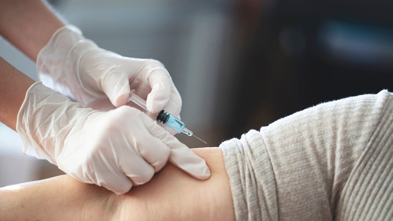 Un patient se fait faire une injection dans le bras par un soignant.