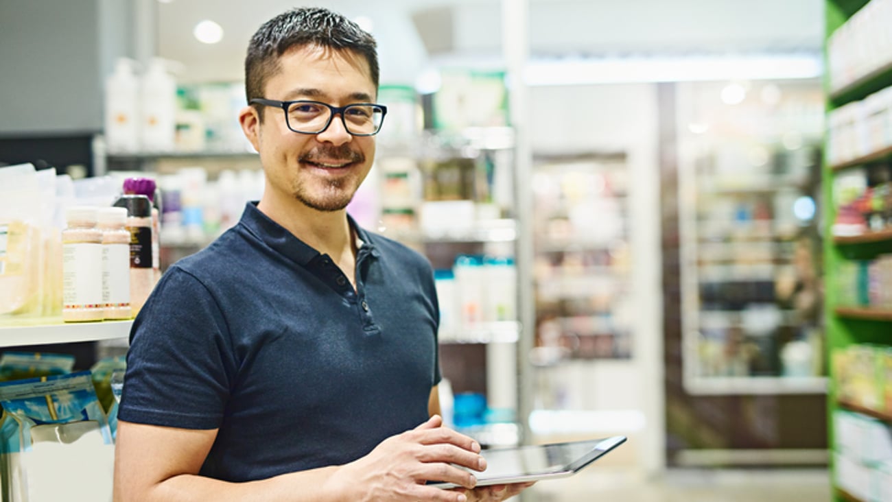 Un pharmacien entrepreneur avec une tablette devant des étagères de médicaments