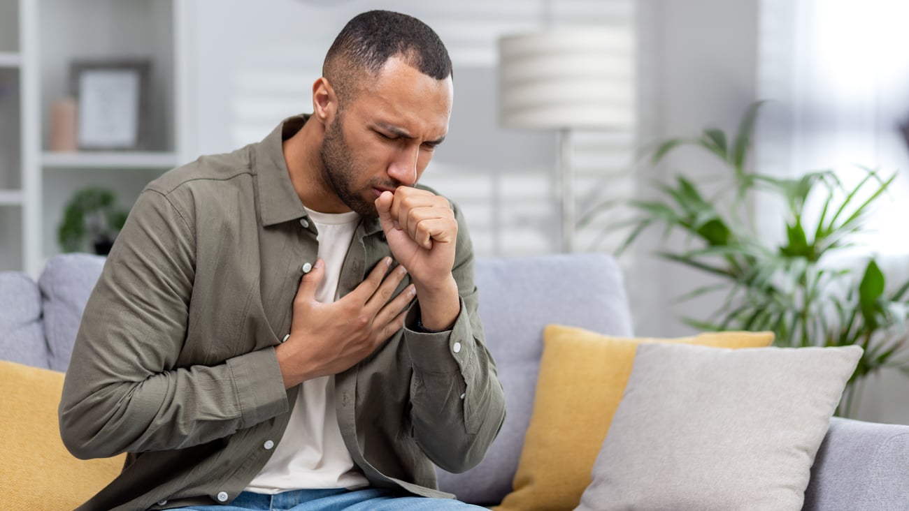 Man with dark skin is coughing into his hand