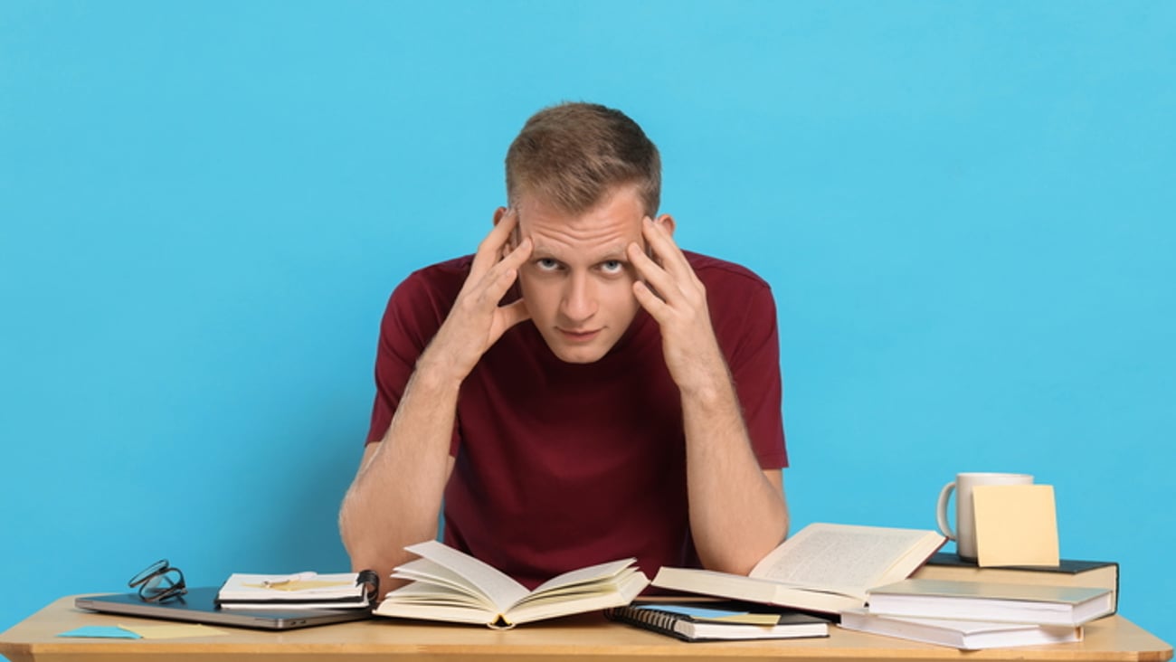 Un jeune homme blanc se tient la tête pendant qu'il étudie.