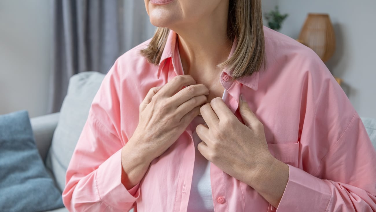 Une femme souffre de bouffées de chaleur pose ses mains sur sa poitrine en signe d'inconfort. 