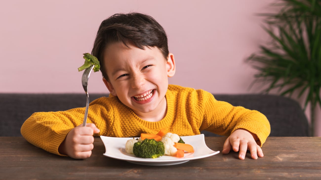 Un enfant mange ses légumes tout sourire.