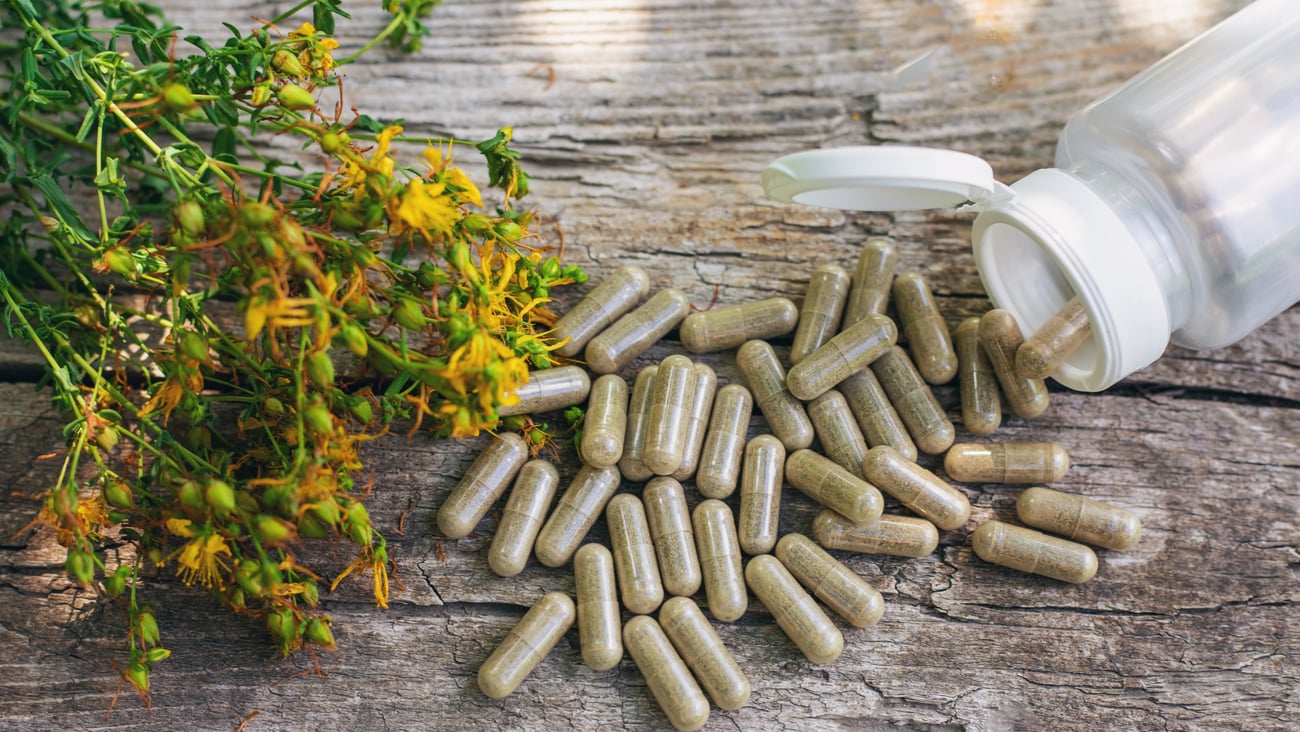  plante de millepertuis à côté d'une cuillère contenant des capsules