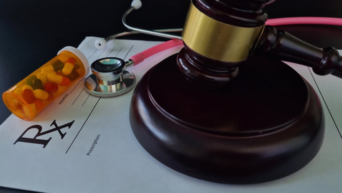 Un maillet de justice posé sur une ordonnance, avec une boîte de médicaments et un stéthoscope