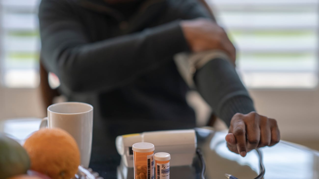 Une personne noire prend sa tension à côté de boîtes de médicaments.