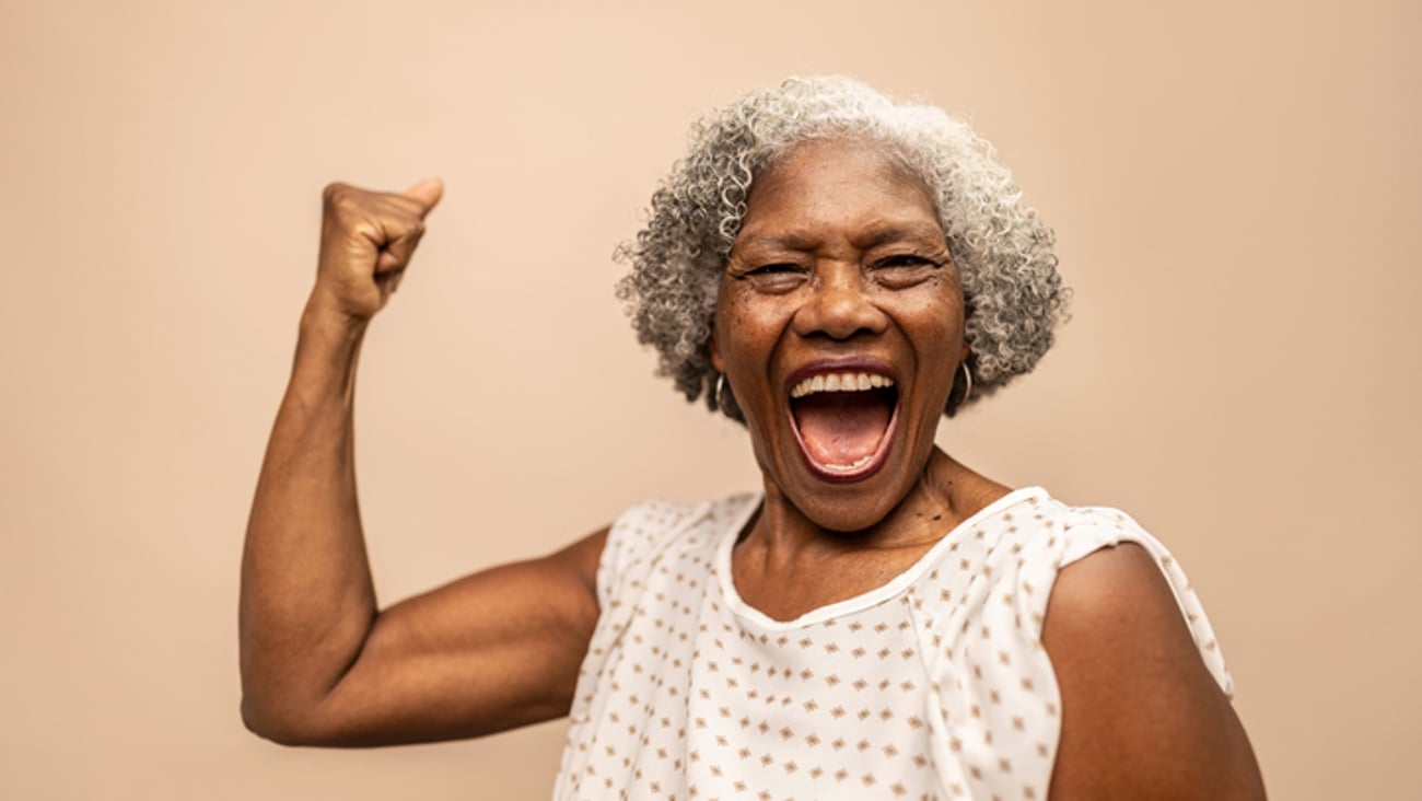Une femme noire âgée sourit en contractant son biceps en signe de force