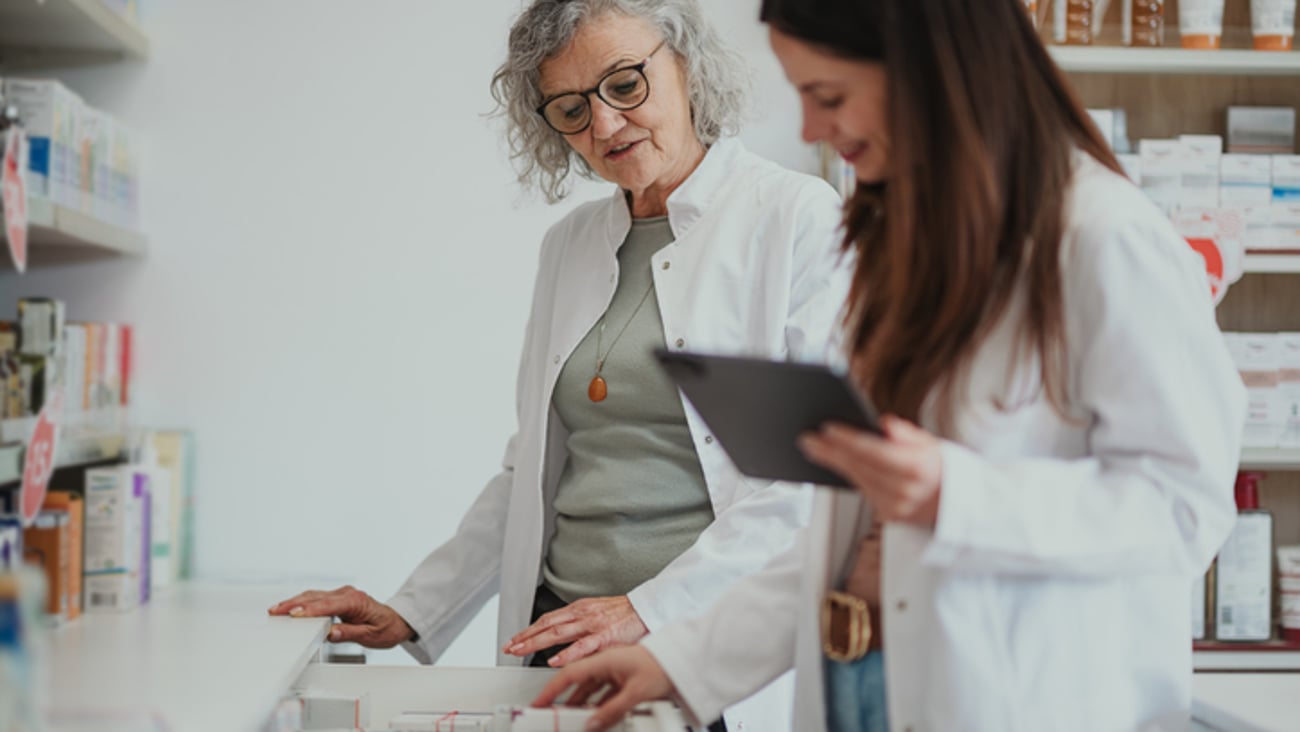 Une pharmacienne âgée et une pharmacienne plus jeune tenant une tablette examinent des médicament