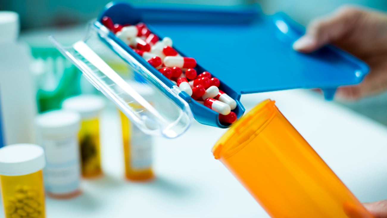 Les mains d'un pharmacien préparant un contenant de médicament en capsule.