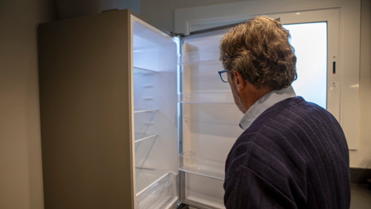 Un homme ouvre un frigo qui est vide, à son domicile.