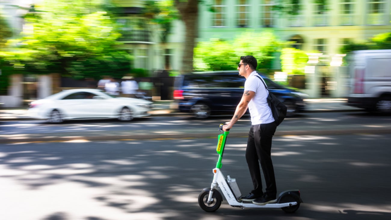 Un jeune adulte sans casque en trottinette électrique.