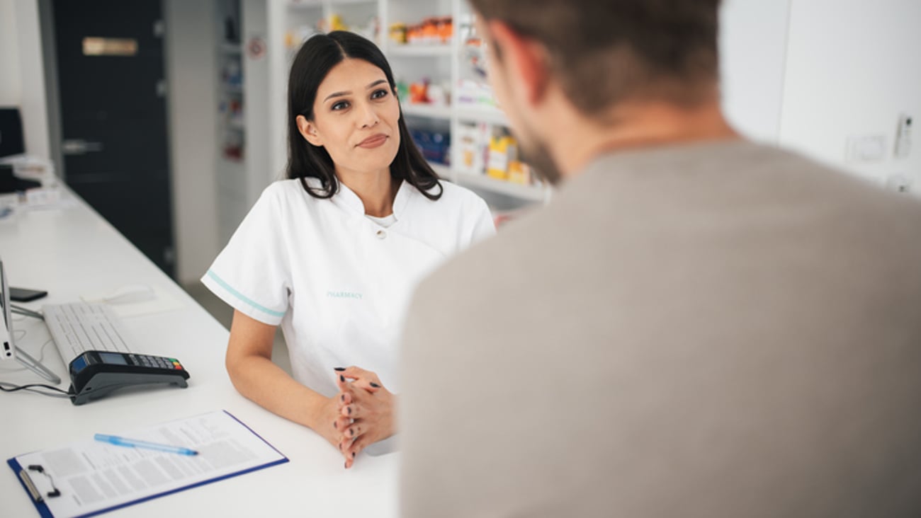 Une pharmacienne discute au comptoir avec un patient homme