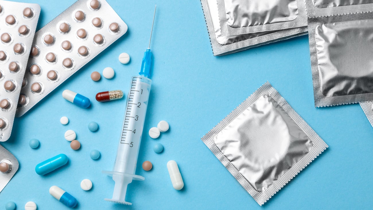 Birth control pills, an injection syringe and condom in a package on blue background. The concept of choosing method of contraception, birth control pills or condom.; Shutterstock ID 1266659281