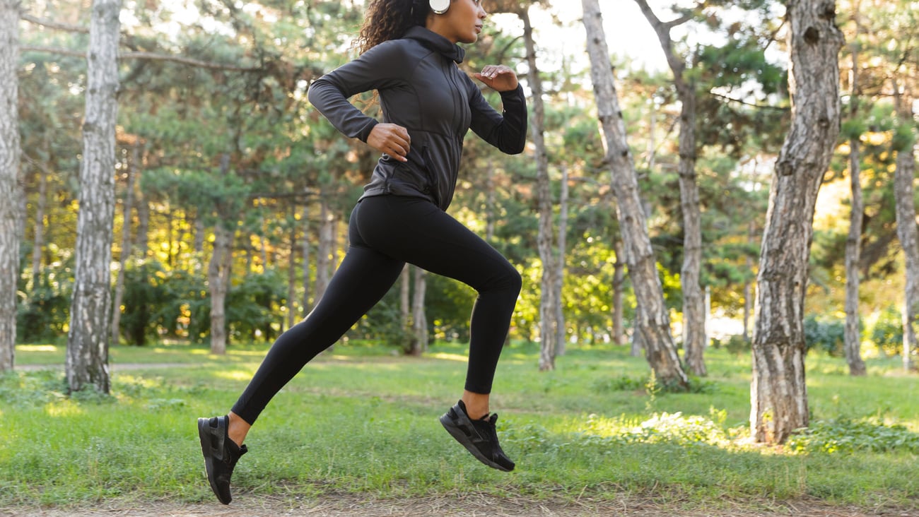 Image of feminine woman 20s wearing black tracksuit and headphones working out while running through green park; Shutterstock ID 1284968125