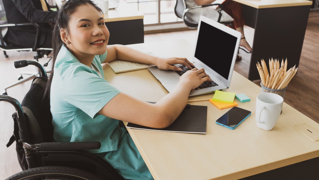 young asian disabled woman with smiling face sitting in the wheelchair and using computer to discuss project with her colleagues in the working office. disability and handicapped concept; Shutterstock ID 1770484058