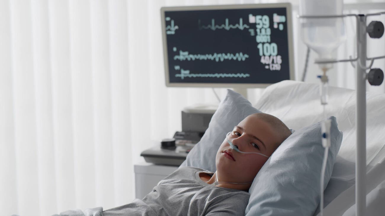 Teenage bald boy lying in hospital with oxygen tube. Side view of kid patient in oncology clinic resting in bed having chemotherapy treatment in ward; Shutterstock ID 1921349135