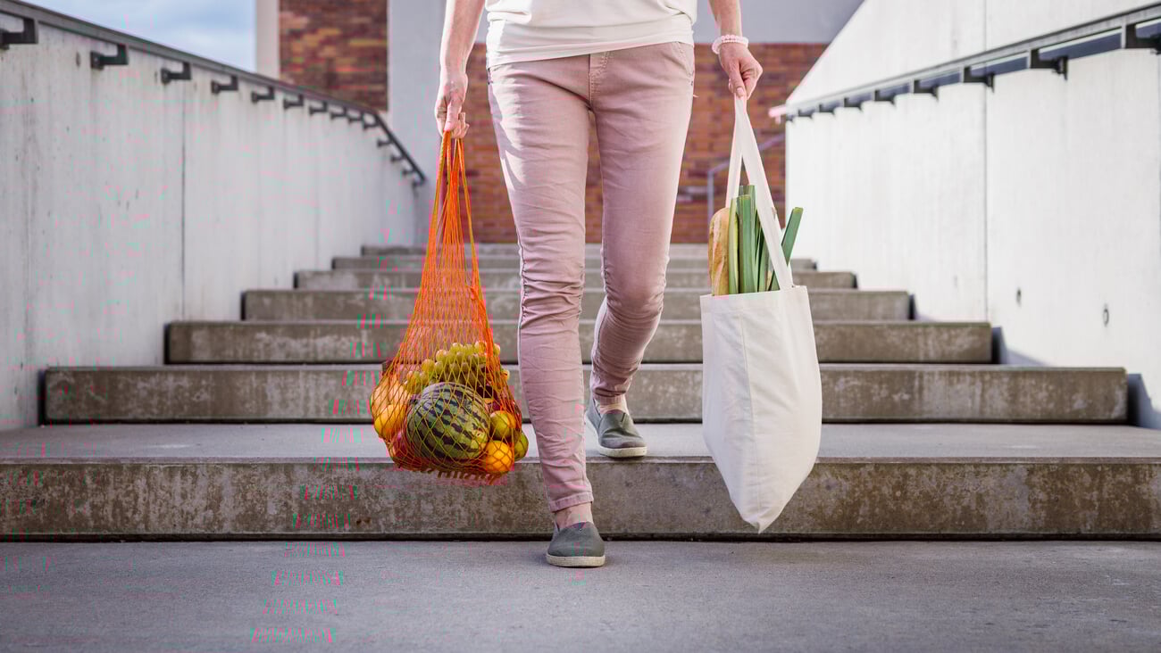 Woman walking at stairs and carrying reusable mesh bag after shopping groceries in city. Sustainable lifestyle with zero waste and plastic free; Shutterstock ID 2024970326