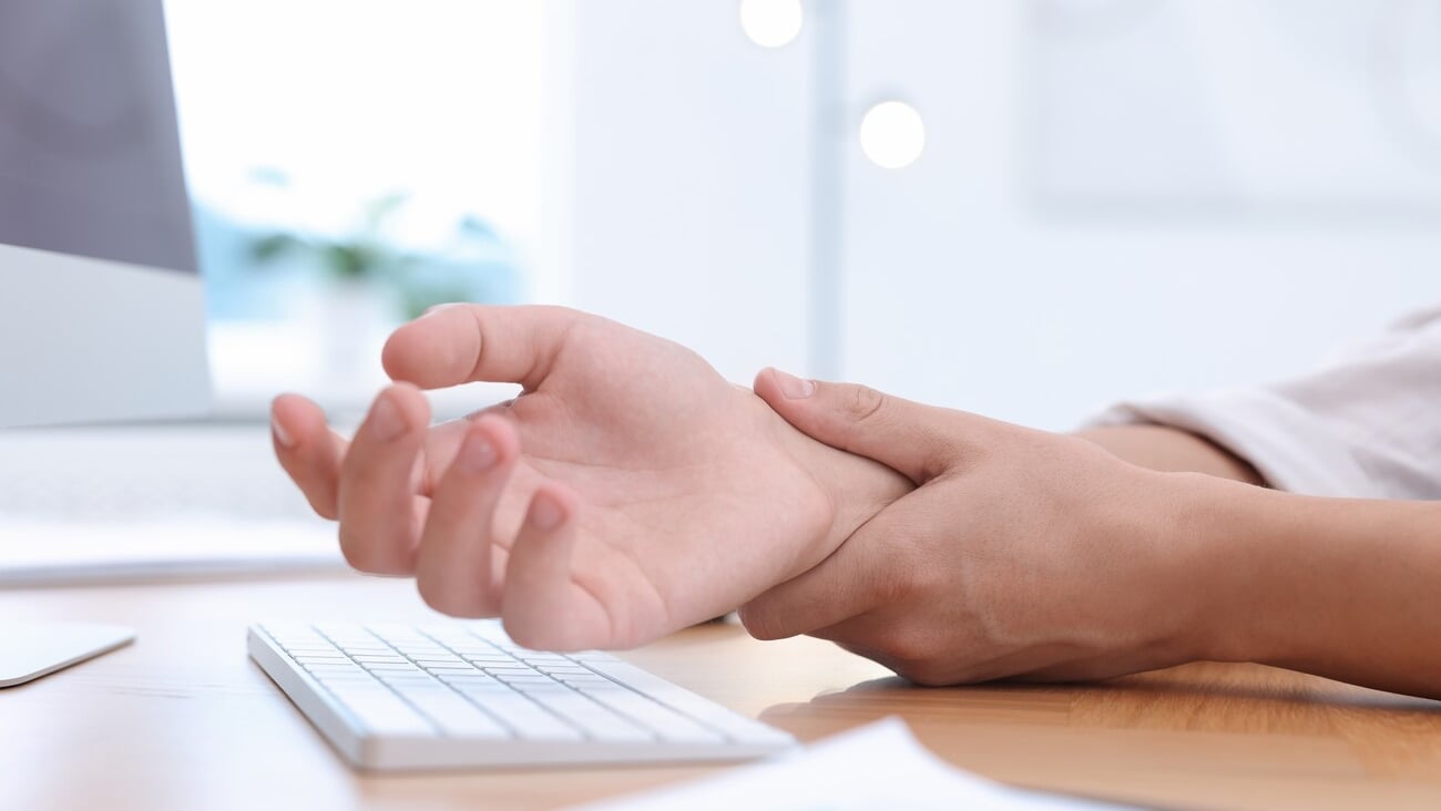 Man suffering from pain in wrist while working on computer at table indoors, closeup. Carpal tunnel syndrome; Shutterstock ID 2518549623