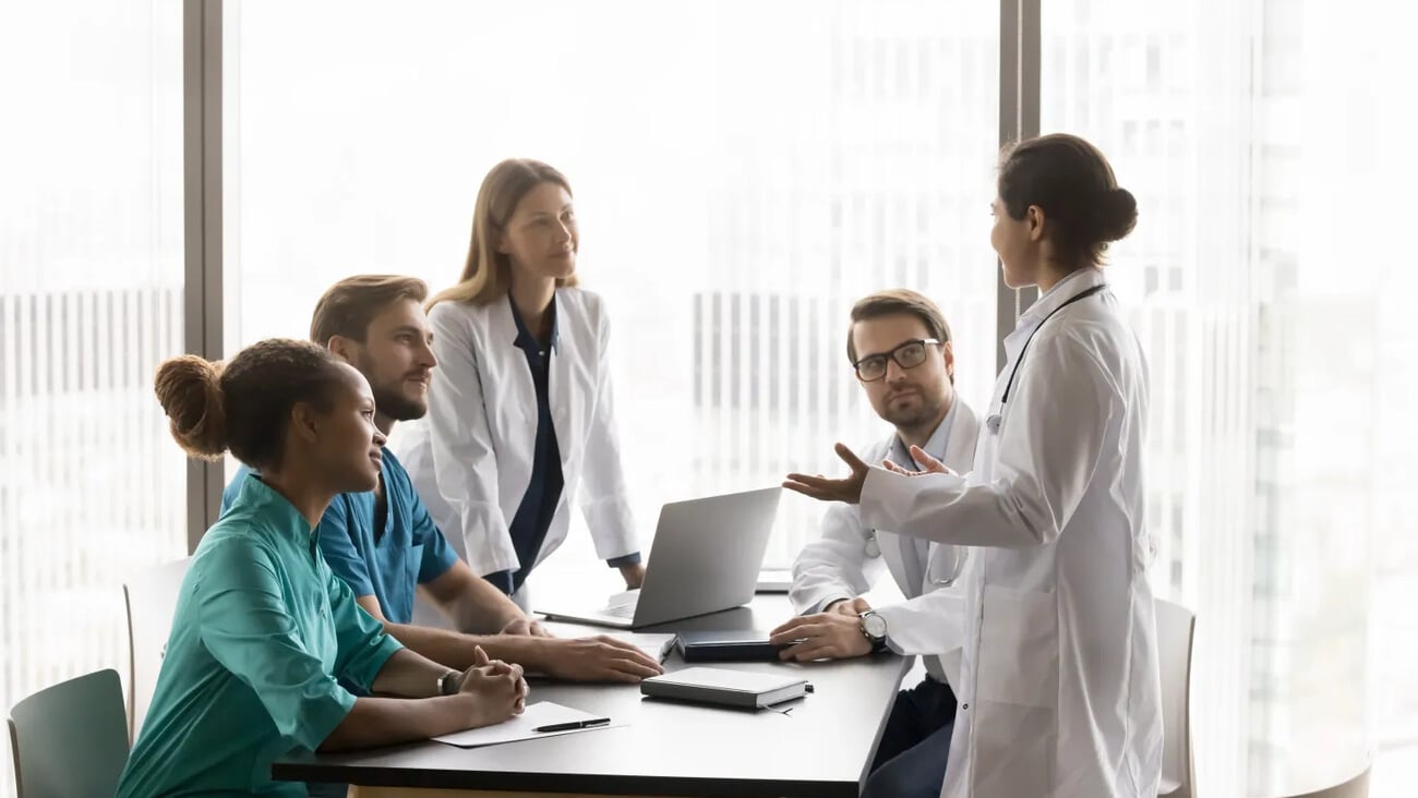 Indian doctor wear white coat perform during medical concilium event with professional colleagues, hospital staff members, provide explanation, offers solutions, during discussion patient disease case; Shutterstock ID 2571102491