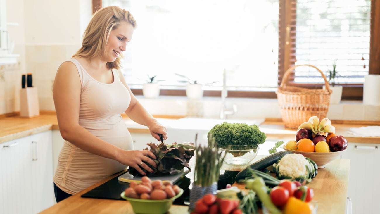 Beautiful pregnant woman preparing meal on kitchen island from fresh ingredients; Shutterstock ID 586437113
