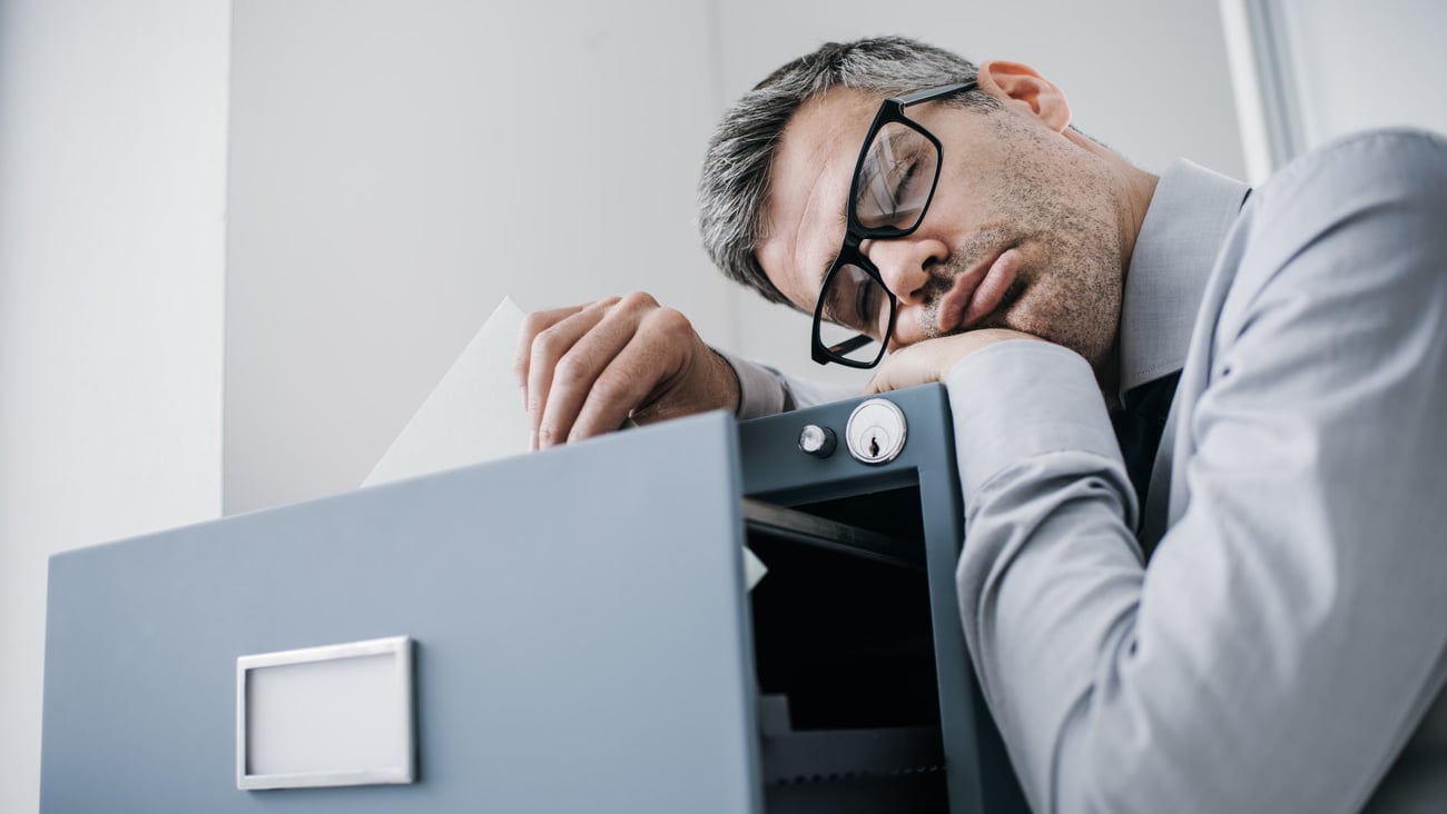 Tired lazy office worker leaning on a filing cabinet and sleeping, he is falling asleep standing up; stress, unproductivity and sleep disorders concept; Shutterstock ID 778064239