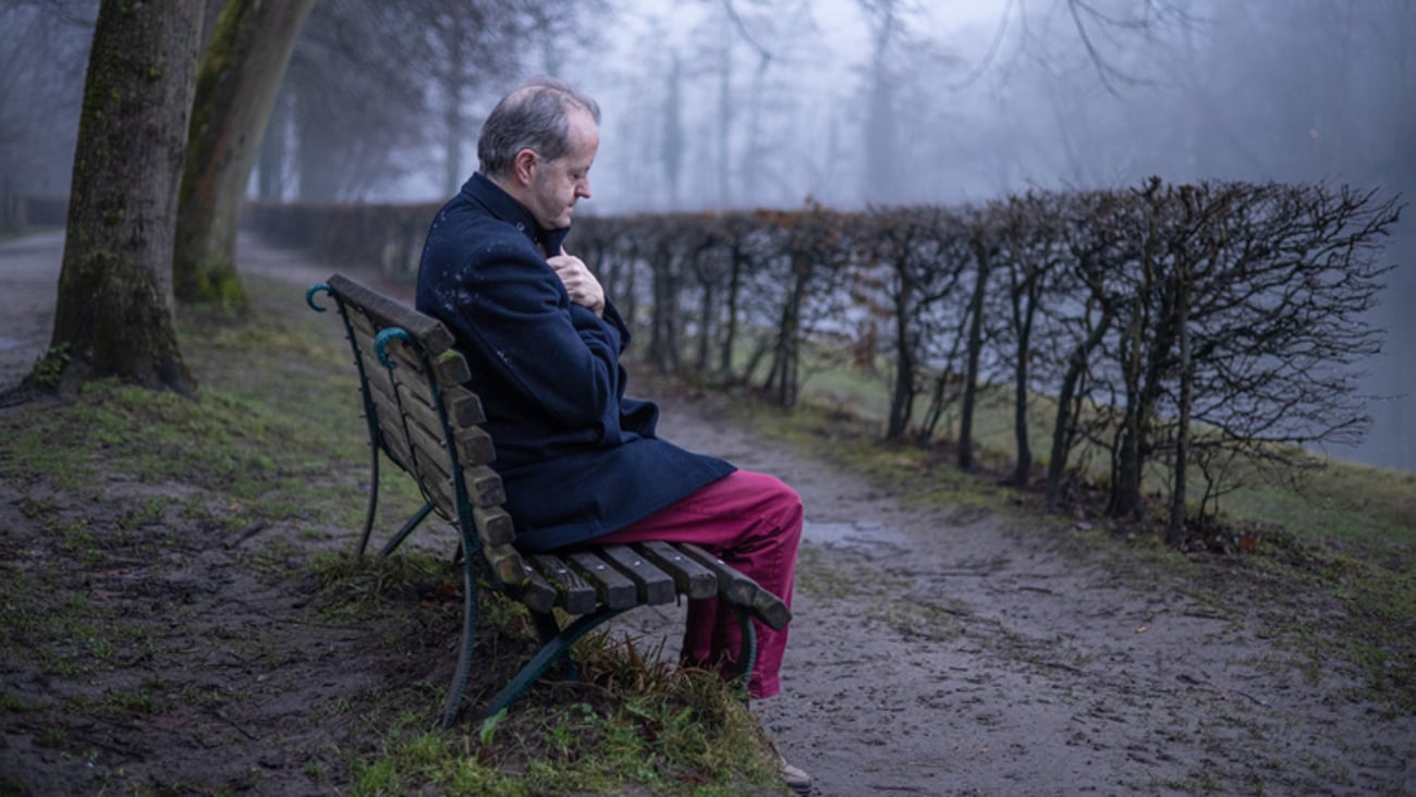 Une personne âgée déprimée est assise sur un banc de parc, lors d'une journée brumeuse.