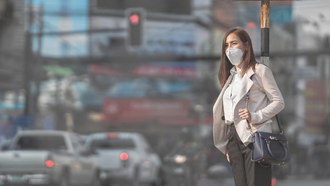 Une femme attendant de traverser une rue achalandée porte un masque.