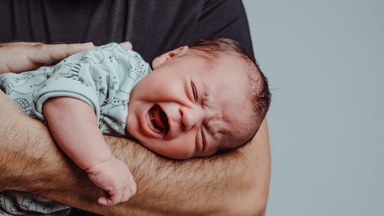 Un bébé pleure dans les bras de son père.