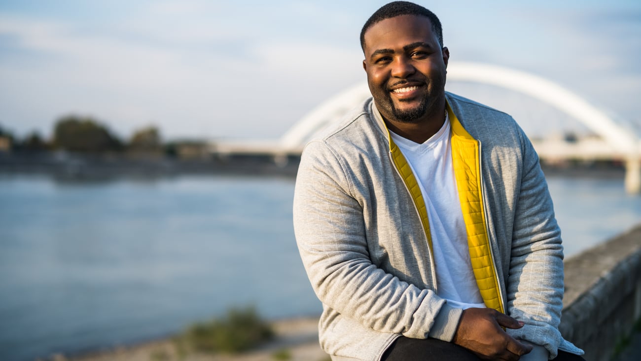 homme noir souriant assis sur un pont