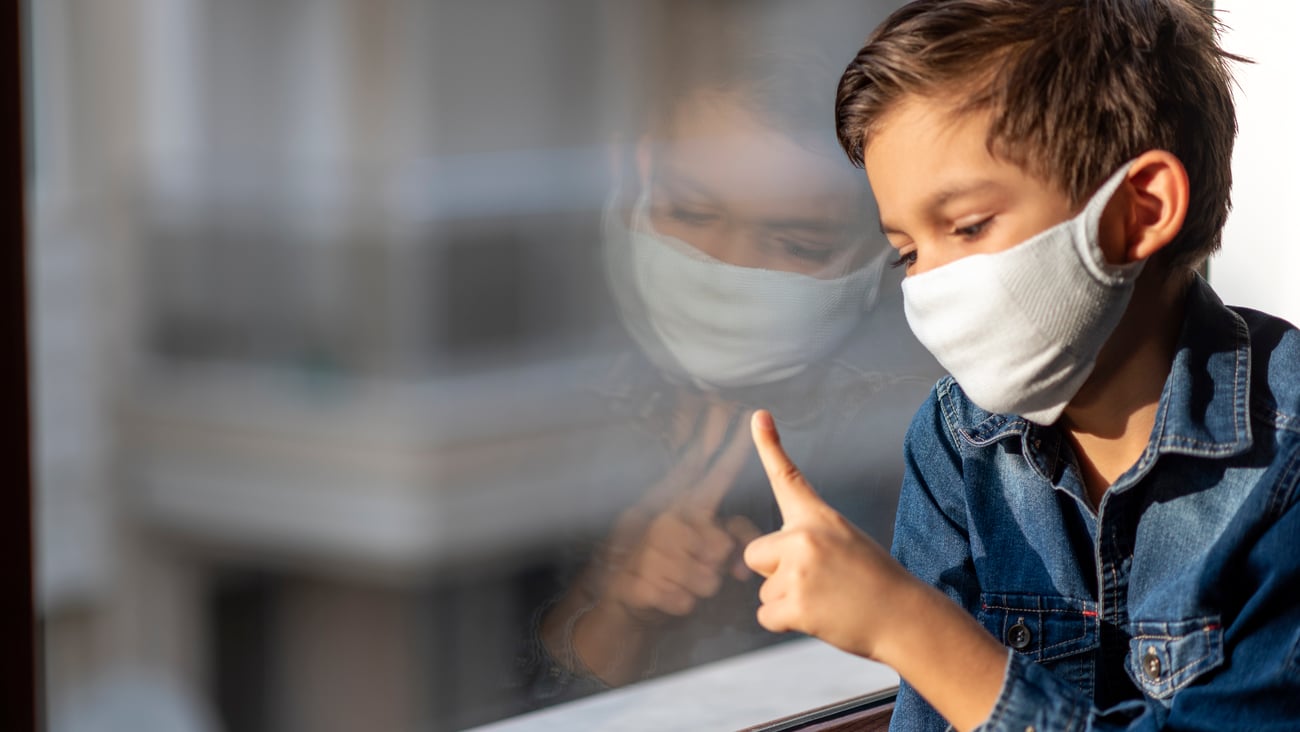 Un enfant malade masqué regarde par une fenêtre
