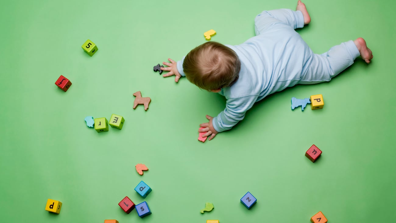 Baby crawling on green floor surrounded by letter toys