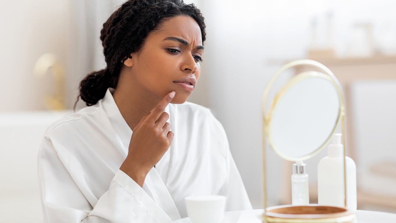 Dark-skinned woman looking at her acne in the mirror