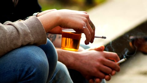 Deux personnes discutent en fumant une cigarette et en buvant de l'alcool.