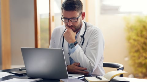 Un médecin en réflexion dans son cabinet, devant son ordinateur.