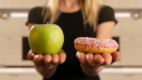 Femme tenant une pomme d'une main et un beigne de l'autre