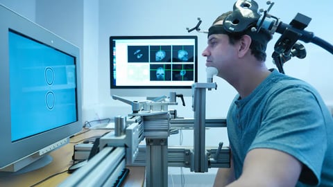 Dispositif de Stimulation Magnétique Transcrânienne (TMS) avec bobine de stimulation en forme de 8 positionnée près de la tête du participant pendant une tâche visuelle. Image Source Trading Ltd/Shutterstock